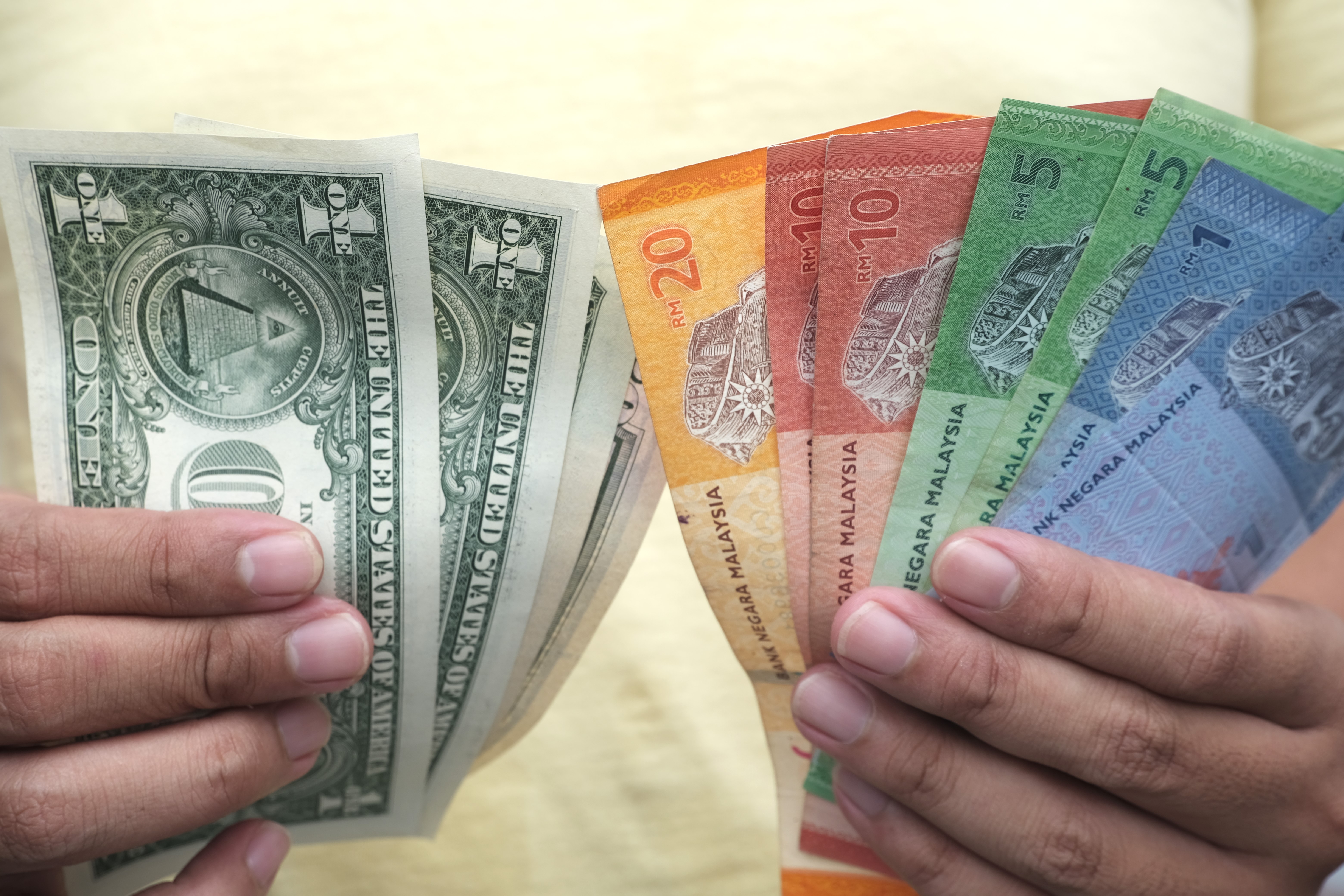 Close-up of hands holding Malaysian ringgit and US dollar banknotes, showing currency exchange, travel finance, and money comparison.