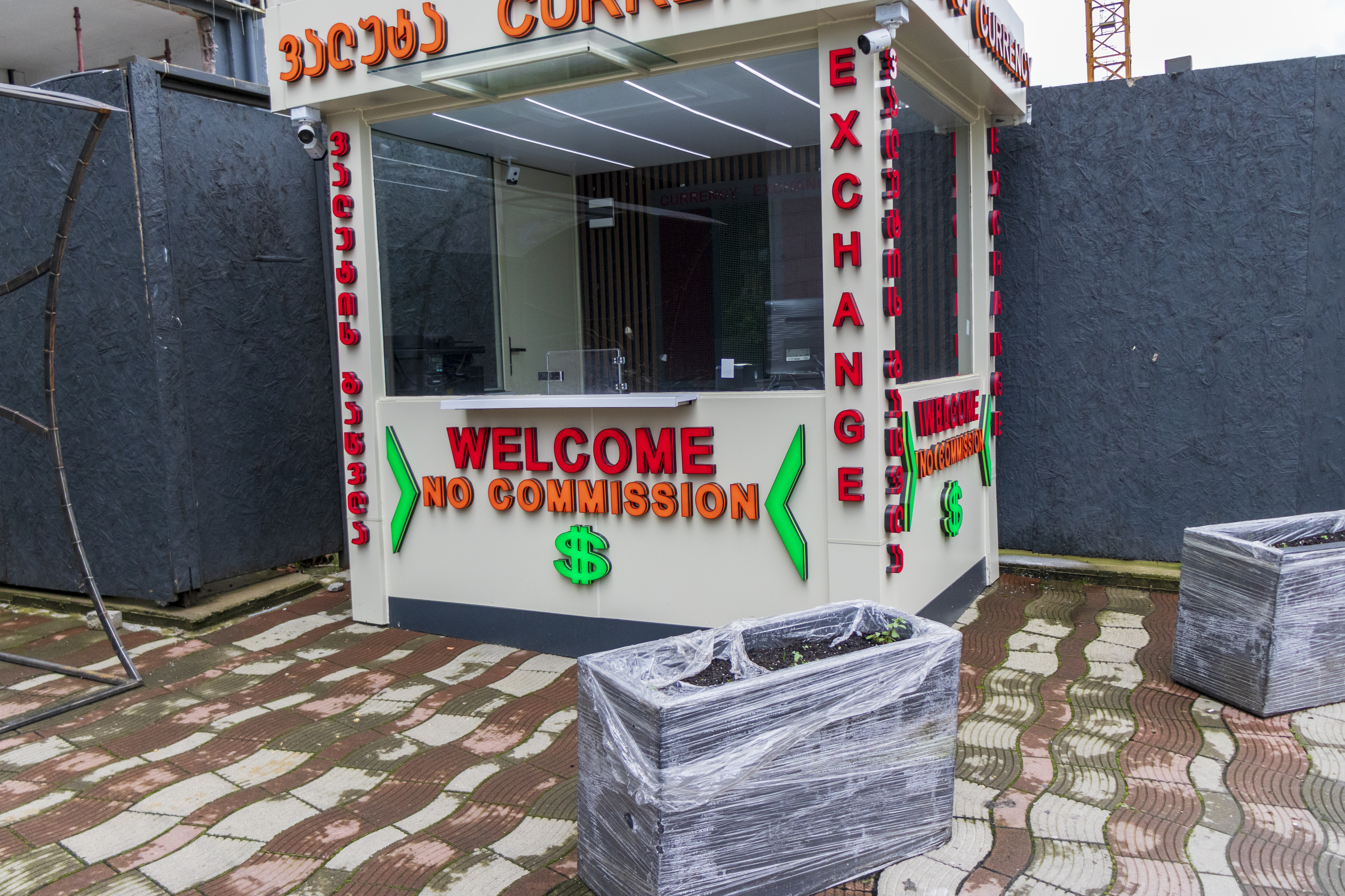 Exterior view of a street-side currency exchange booth with red and green neon signage. Money
